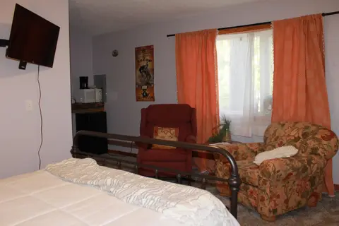 Queen bed facing two armchairs and a wall-mounted TV