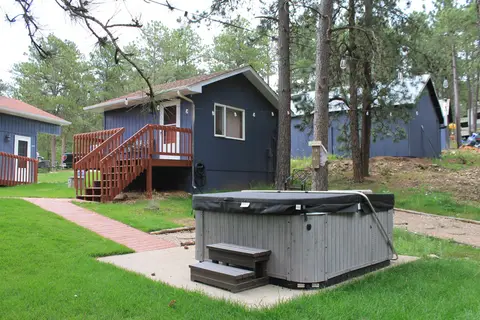 Small blue cabin with wooden steps, beside a covered hot tub on the lawn