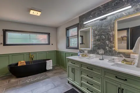 Primary bathroom with a black freestanding tub and a green double vanity