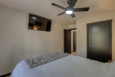 Queen bedroom with a wall-mounted TV and a ceiling fan