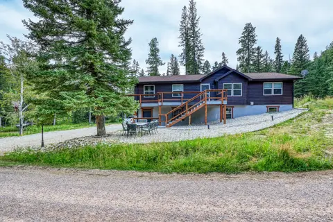 House from the road, with a spruce, a patio table, and stairs up to the deck