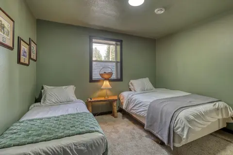 Lower-level bedroom with two beds, a bedside lamp, and framed prints