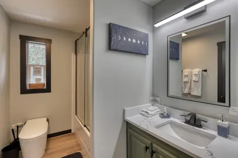 Bathroom with a green vanity, a toilet, and a tub with glass doors