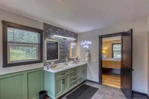 Primary bathroom with a green double vanity and lighted mirrors