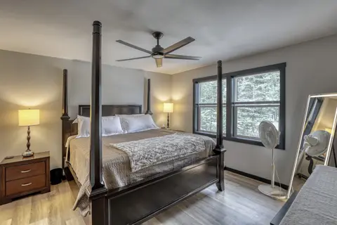 King bedroom with a dark four-poster bed, two lamps, and windows to the trees