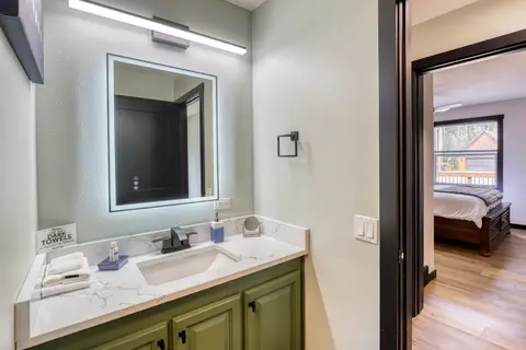 Bathroom with a green vanity and a lighted mirror, next to a bedroom