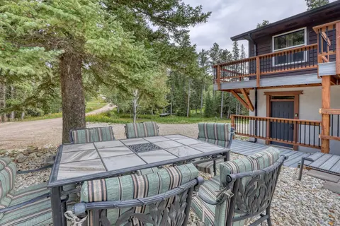 Patio table with cushioned chairs on gravel under a spruce, below the deck