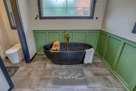Black freestanding tub against green wainscoting on a tile floor