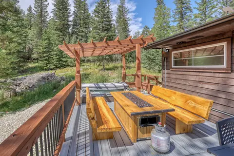 Fire table with log benches under a pergola, next to the covered hot tub
