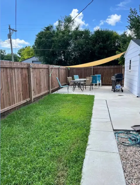 Backyard patio with a table and chairs under a shade sail, a grill, and a wood fence
