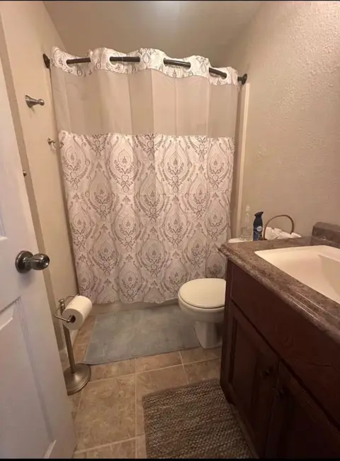 Bathroom with a tub and patterned shower curtain, a toilet, and a dark wood vanity