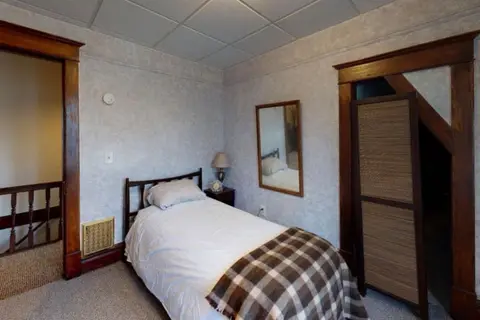 Twin bed with a plaid throw beside a stair railing, with a mirror on the wall