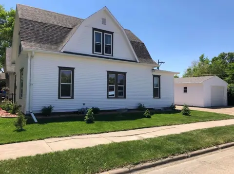 White house with a gambrel roof, a front lawn, and a detached garage