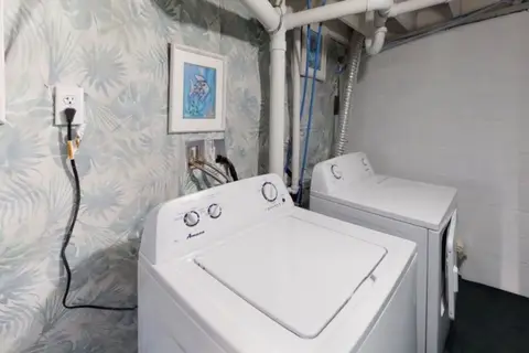 Laundry area with a white washer and dryer under exposed pipes
