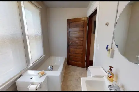 Bathroom with a tub beneath two shaded windows and a pedestal sink