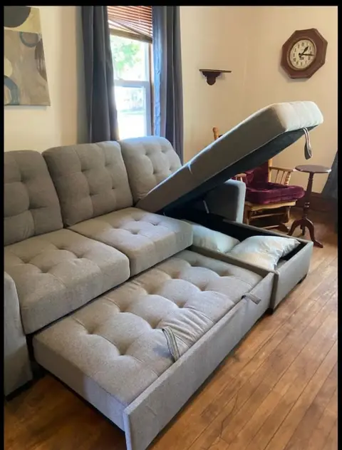 Gray tufted sectional with its pull-out bed open and a lift-up storage chaise