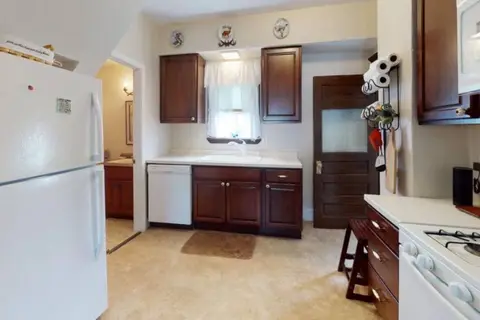 Kitchen with a white refrigerator, a dishwasher, and wood cabinets under a curtained window