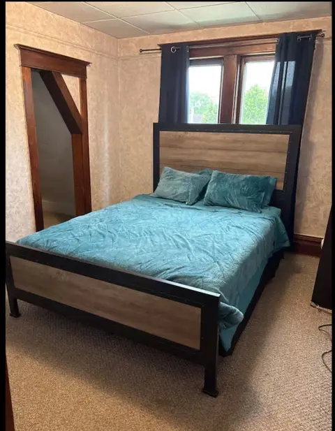 Bedroom with a wood-panel bed, teal bedding, and dark curtains at a double window