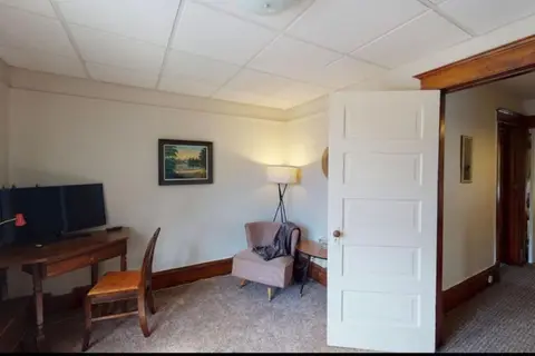 Room with a desk and monitor, a wooden chair, and a pink armchair by a floor lamp