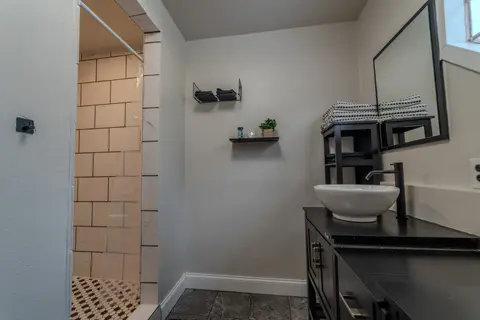 Tiled walk-in shower beside a black vanity with a vessel sink