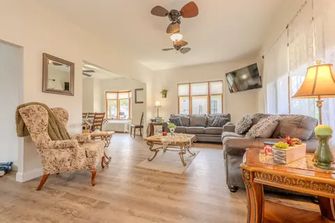 Living room with two gray sofas, a wingback chair, a wall-mounted TV, and a view into the dining area