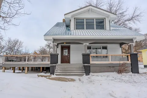 Front of the white house with a covered porch, a metal roof, and a dormer window