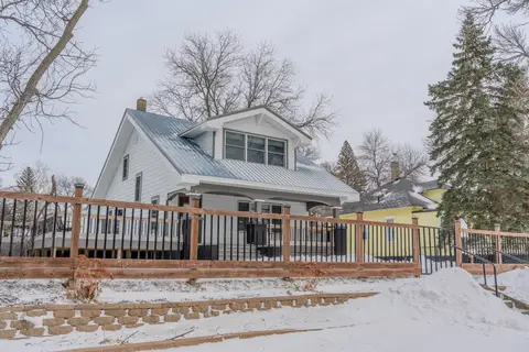 White house with a metal roof behind a wood and black-rail fence, in snow