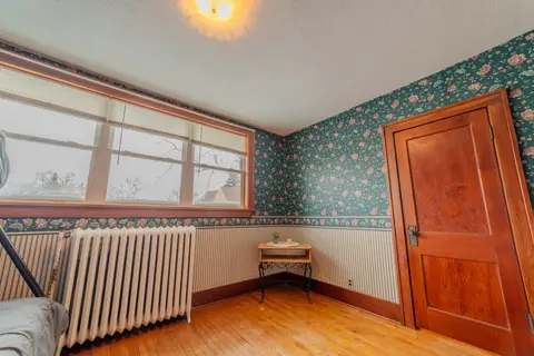 Green floral bedroom with a radiator, a wide window, and a wood door