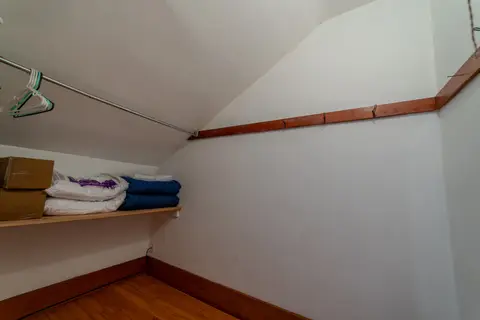 Closet with folded blankets on a shelf under a sloped ceiling