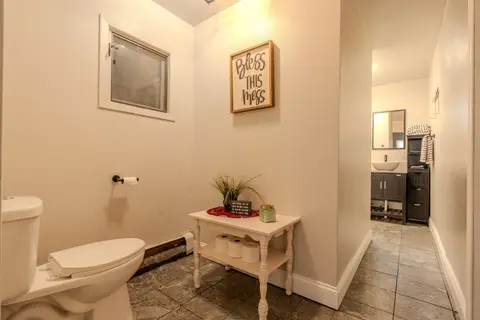 Bathroom with a toilet, a small white table, and a framed sign