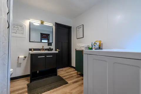 Bathroom with a black vanity, a lit mirror, and a white laundry machine