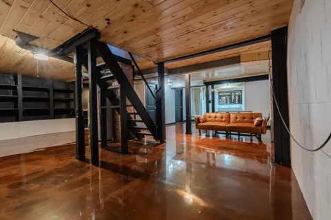 Lower level with a glossy floor, open stairs, shelving, and a leather futon