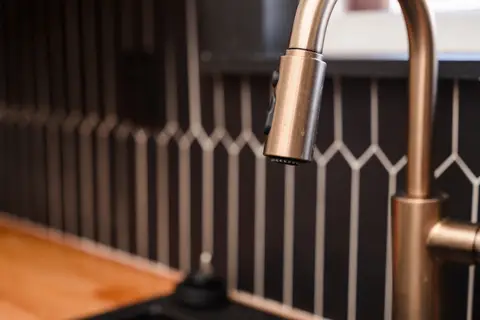 Brass faucet in front of a dark picket tile backsplash