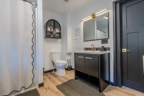 Bathroom with a black vanity, a lit mirror, and a shower curtain