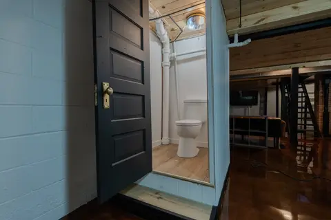 Small lower-level room with a toilet, behind a black paneled door