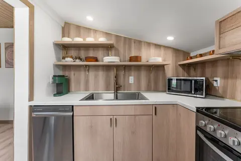 Kitchen with open wood shelves, a sink, dishwasher, and microwave