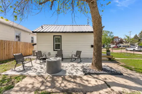 Patio with rocking chairs around a round fire pit, under a large tree