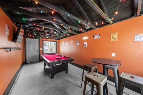 Shared game room with a pool table, bistro table, and stools under string lights
