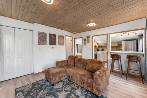 Living room with a wood plank ceiling, a brown corduroy sectional, and bar stools at the pass-through