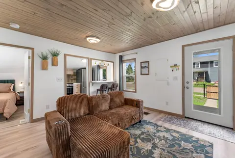Living room with a corduroy sectional under a wood plank ceiling, by the front door and bedroom