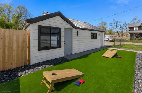 Turf side yard with two cornhole boards beside a white building