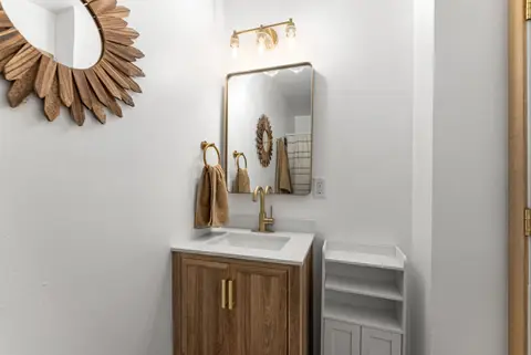 Wood vanity under a brass mirror and a sunburst mirror