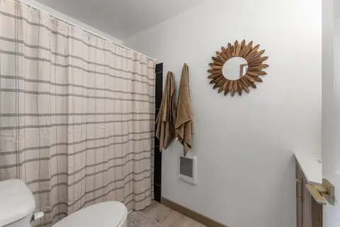 Bathroom with a plaid shower curtain, towels, and a sunburst mirror