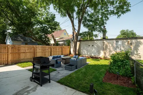 Backyard with outdoor seating, a grill, landscaped garden beds, and mature shade trees