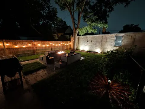 Private backyard at night with string lights, outdoor seating, and a glowing fire table