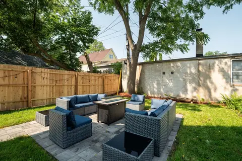 Private backyard patio with lounge seating, a fire table, a green lawn, and shade from mature trees