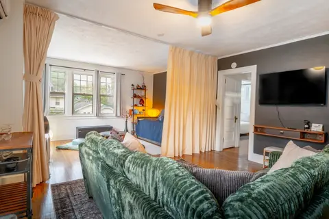 Living room with a wall of windows over the street and a curtain-divided sleeping alcove