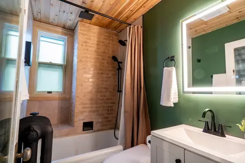 Bathroom with an exposed brick tub surround, rain and handheld shower heads, and a backlit mirror