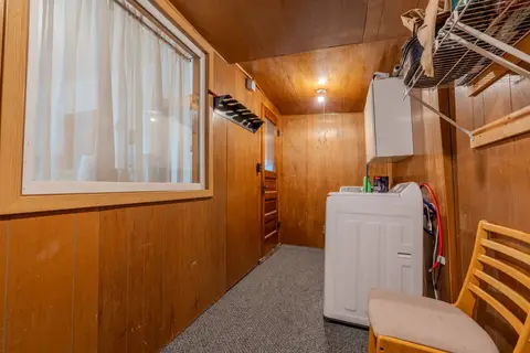 Laundry room with a washer, a wall cabinet, a chair, and a curtained window