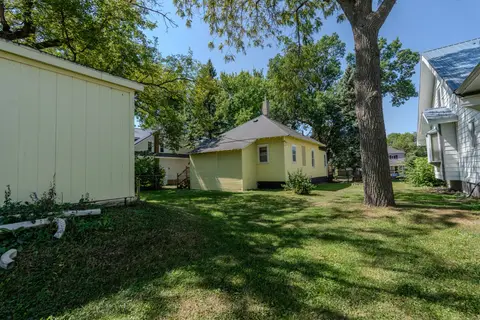 Yellow house seen across the backyard lawn, with a large shade tree